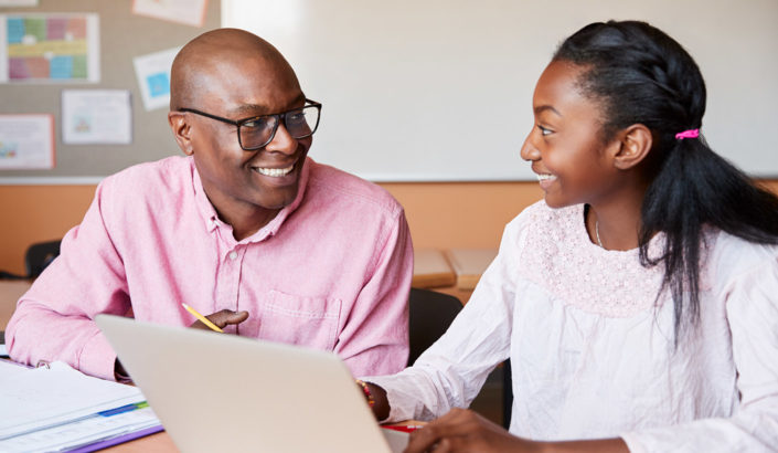 Teacher smiling at student while working at a laptop