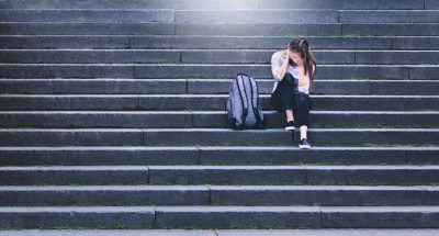 Student sitting on stairs covering face.