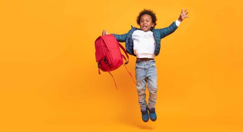A Black girl jumping while holding a backpack