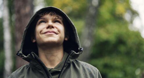 Portrait of a cute teenage boy hiker on a rainy autumn day. The boy is smiling and looking up.