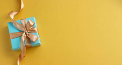 Small blue box tied with gold ribbon on yellow background