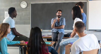 Young teacher talking with teenager students seating in a circle at school