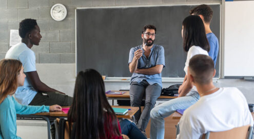 Young teacher talking with teenager students seating in a circle at school