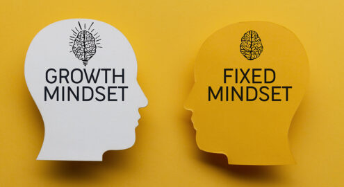 Two paper heads on yellow background. One has growth mindset written on it and one has fixed mindset.