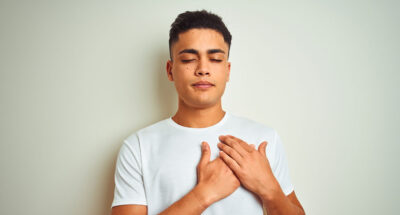 Young latino man holds hands over heart in an effort to practice self-kindness