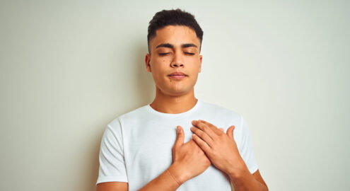 Young latino man holds hands over heart in an effort to practice self-kindness