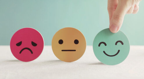 Three paper faces lined up in a row: one red frowning, one yellow neutral, and one green happy
