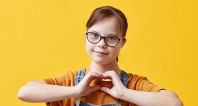 Adolescent student with Down syndrome makes a heart with her hands to symbol self-love and compassion