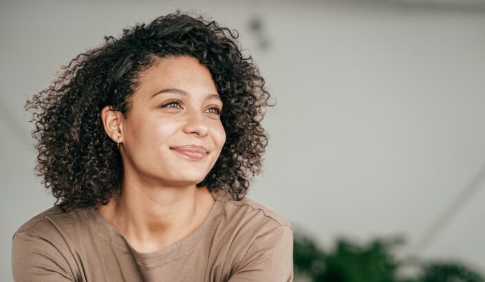 Black woman in a camel colored shirt sits with a content smile