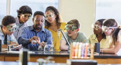 A Black man in his 50s teaching a multi-ethnic group of teenagers in a high school science class.