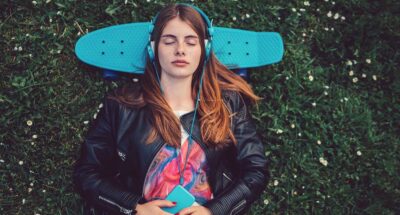 Young white woman lying down in the grass with skateboard behind head and listening to mindfulness practice