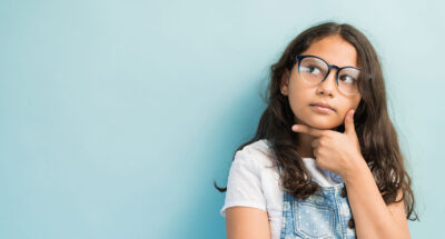 Thoughtful female child with hand on chin looking away against turquoise background