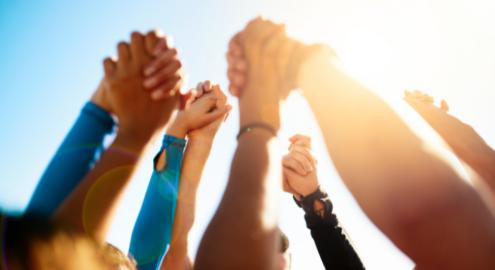 Uplifted hands together against blue sky and sunlight