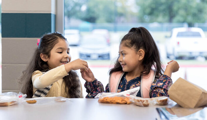 Two children sitting at a table, sharing snacks and smiling.