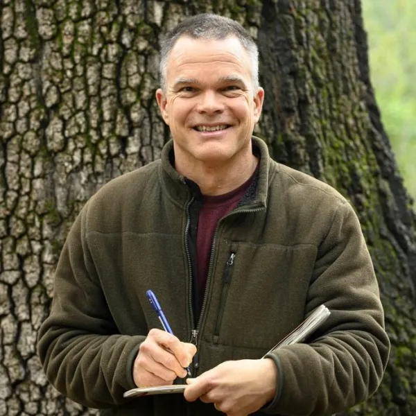 Photograph of man looking at the camera and smiling with notebook and pencil