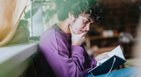 Young man engrossed in a book within a cozy indoor setting