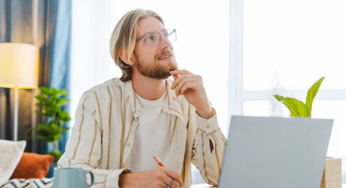Young professional with a beard and glasses is deep in thought, reflecting in his journal.