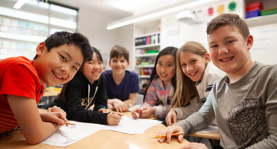 A group of six children smiling and working together at a classroom table.