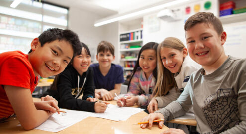 A group of six children smiling and working together at a classroom table.