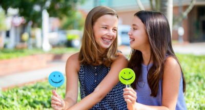 Two tweens with long hair and braces share smiley-face candies with each other.