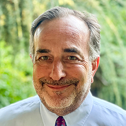 Photograph of happy smiling man in suit in front of nature smiling at camera