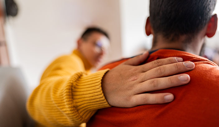 Person in a yellow sweater giving an empathic touch to a person in a red shirt.